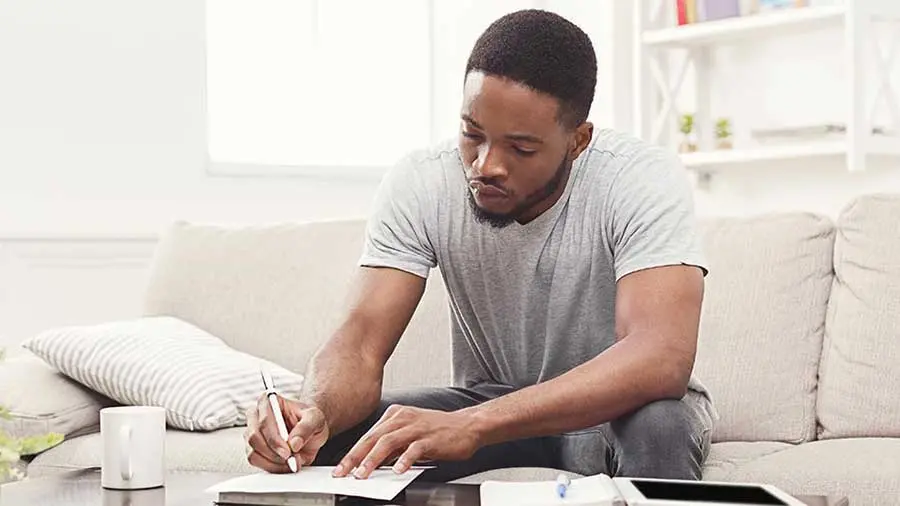 A man writing on a couch focusing on understanding creditworthiness)