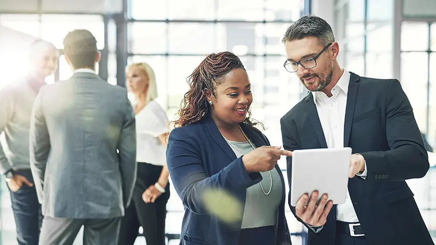 Two professional coworkers standing and looking at a tablet device together.