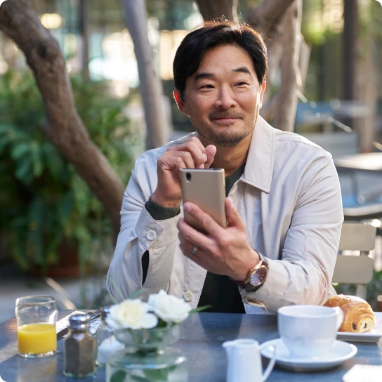 Man seated and relaxed in an outdoor cafe using a smartphone
