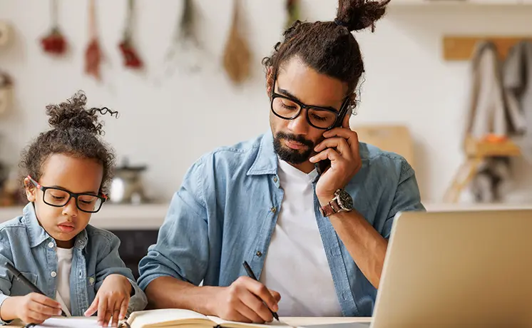 Child writing next to parent working at home