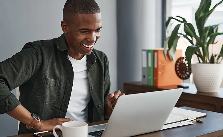 Young adult sitting at a desk in front of a laptop smiling