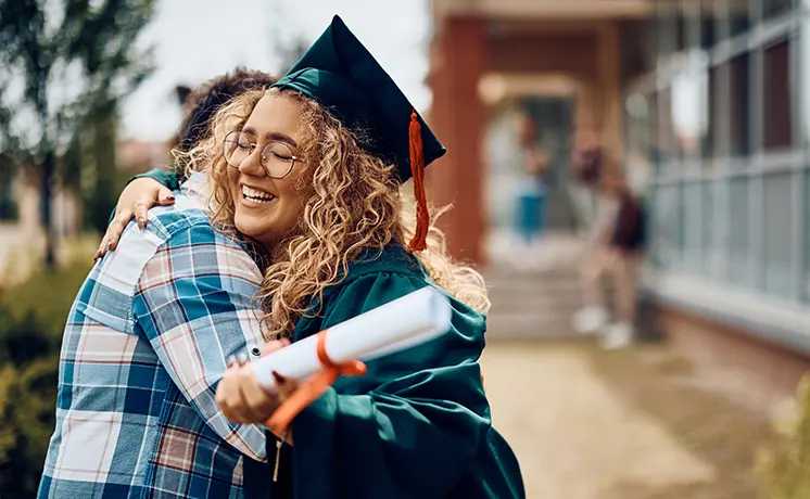 Graduate holding a diploma while being hugged at a cap and gown ceremony