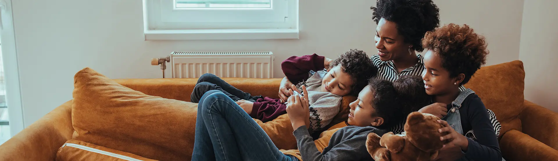 Happy mom and three kids relaxing on a sofa looking at a phone held by one of the children