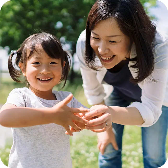 Happy preschool child playing outside sharing a moment with smiling mom leaning over to look at something in the child's hands
