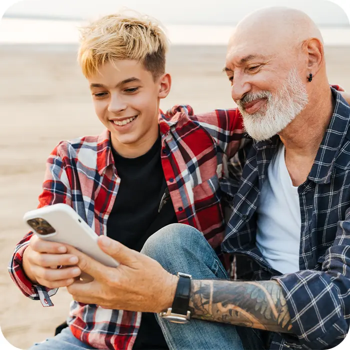 Teen and father at the beach smiling while sharing a moment looking at a phone