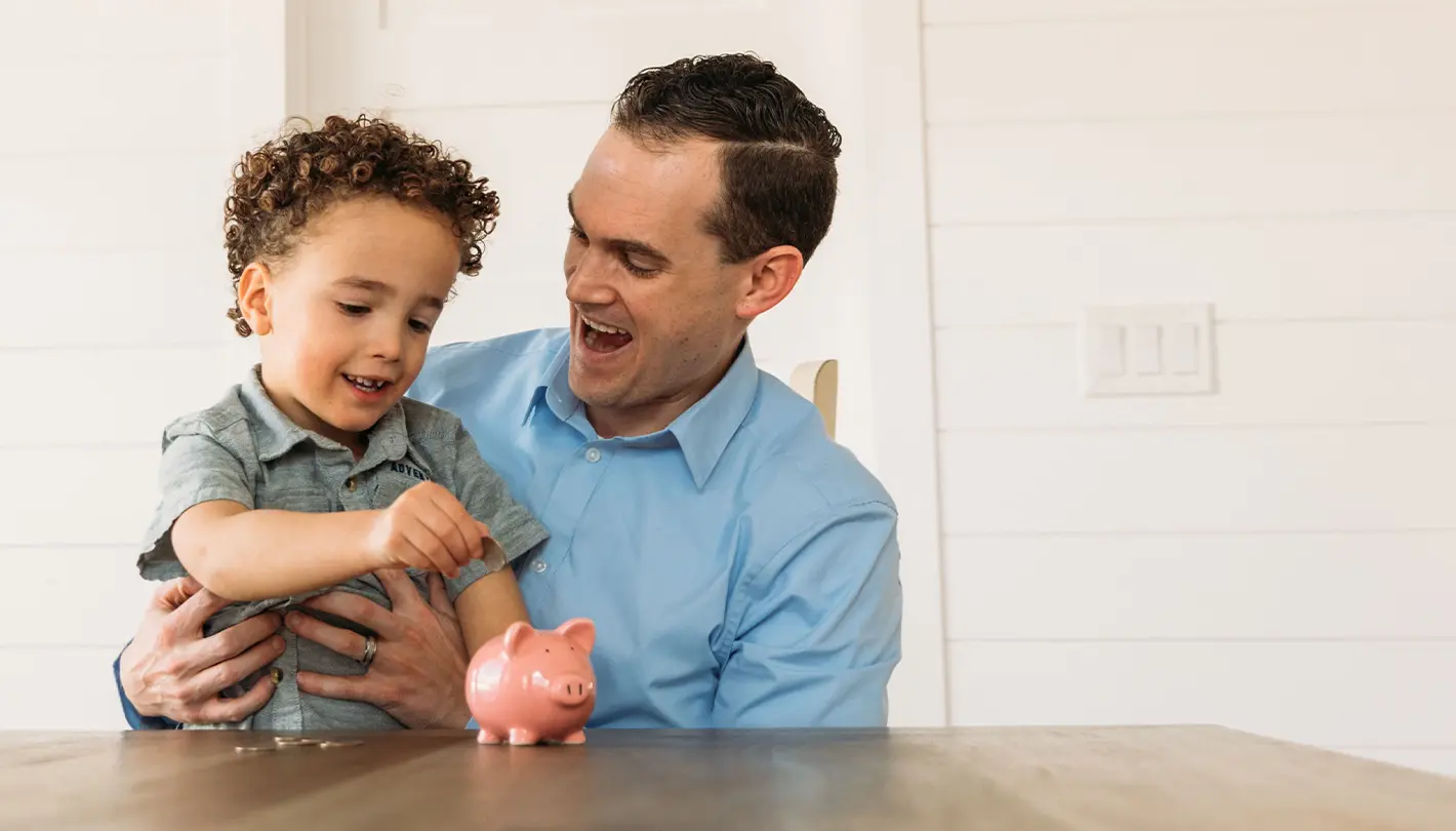 Dad holding his young son placing coins in a piggy bank to build a special nest egg