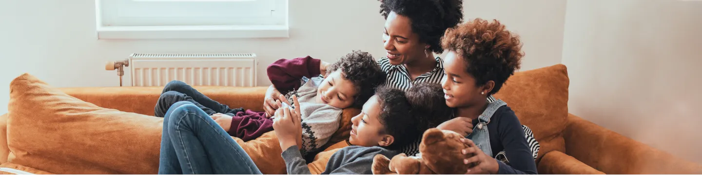 Happy mom and three kids relaxing on a sofa looking at a phone held by one of the children