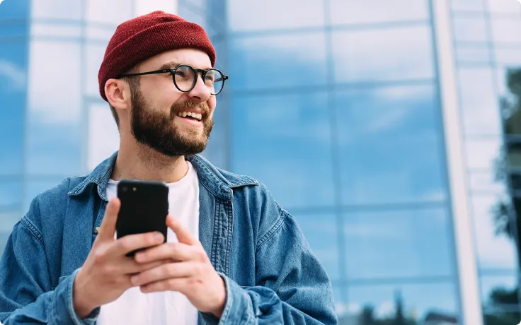 Man wearing hat and glasses holding mobile phone and smiling