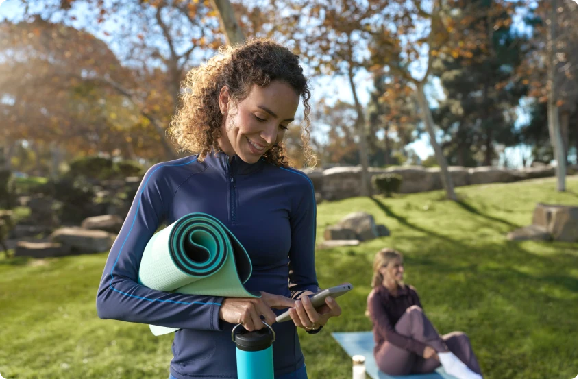Woman standing in a park using a smartphone after an outdoor yoga class