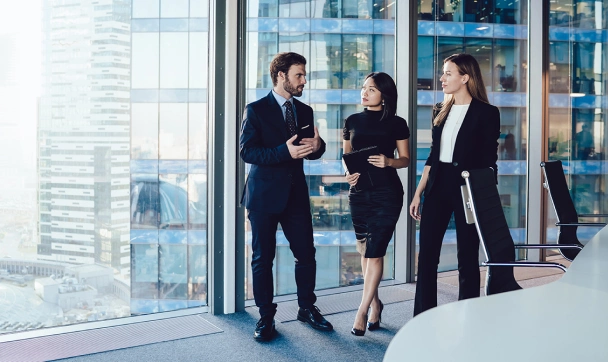 Professional colleagues, two women and a man, wearing business suits and standing in a large office