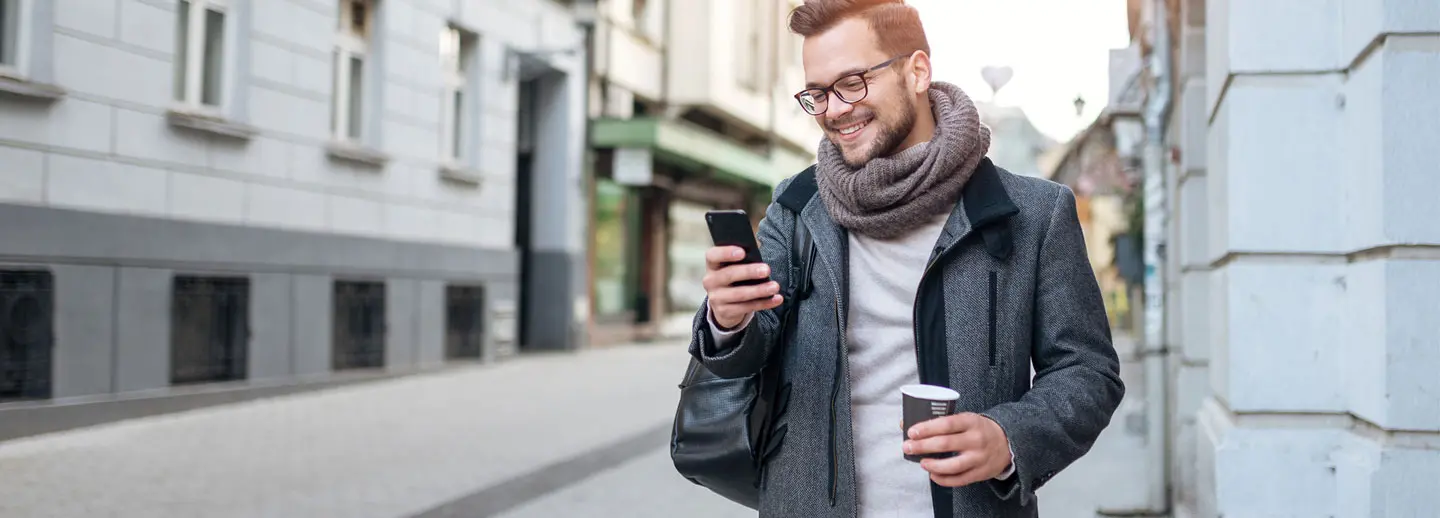 man smiling at phone while walking down the street