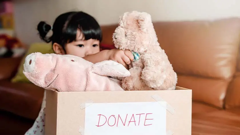 young child adding her stuffies to a donation box