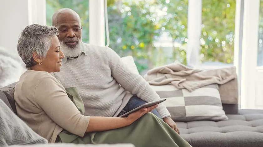 senior couple sitting on couch looking at an iPad