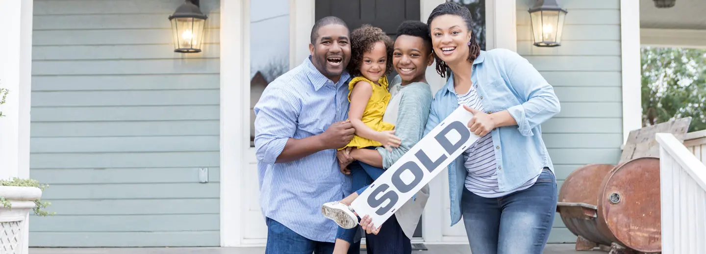family standing outside new home with a sold sign