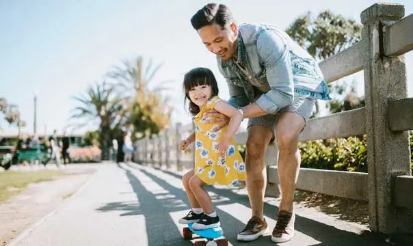 Young father teaches daughter how to skateboard