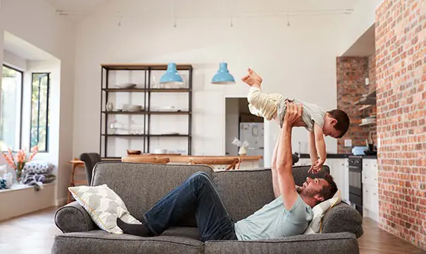 Young father hold baby over him on couch in living room