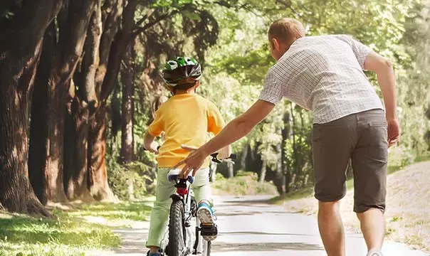 father pushing sons bike while teaching him to ride