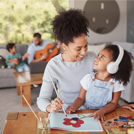 Young mother painting a flower with her daughter sitting on her lap