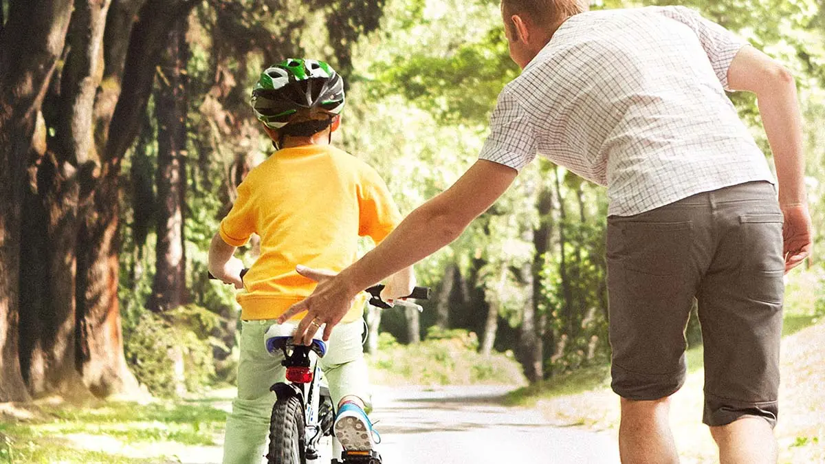father helping child learn how to ride a bike