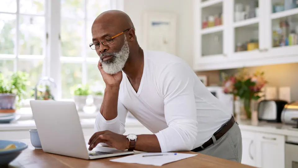 Bearded man with glasses using a laptop in his kitchen