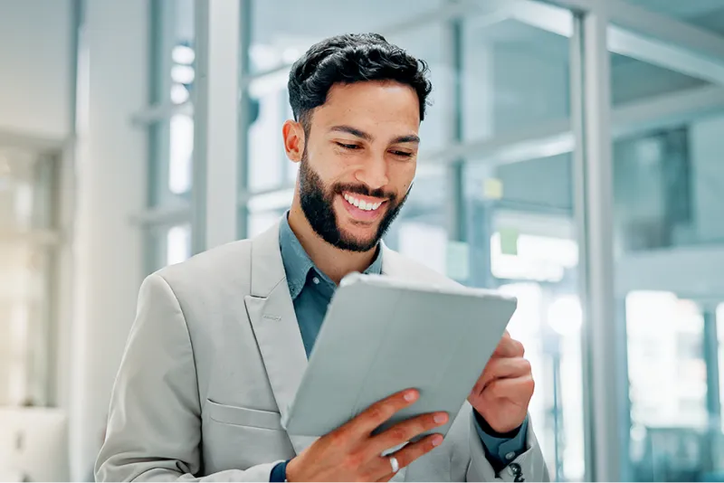 Young man wearing a suit and smiling while looking at a tablet device
