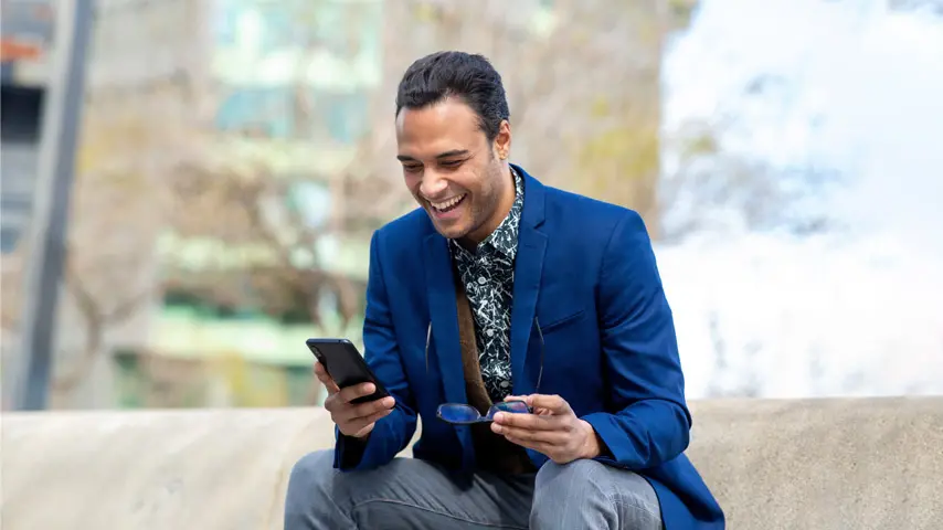 Smiling man wearing a blazer and using his phone to trade stocks
