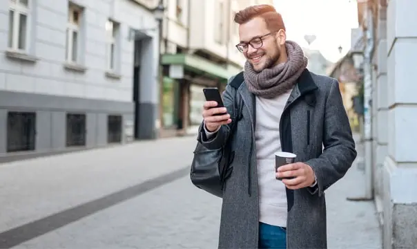 man in scarf walks down street while looking at phone