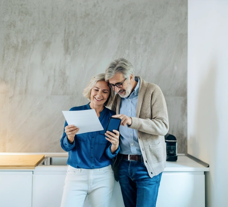 Older couple standing in their kitchen and looking at investment paperwork