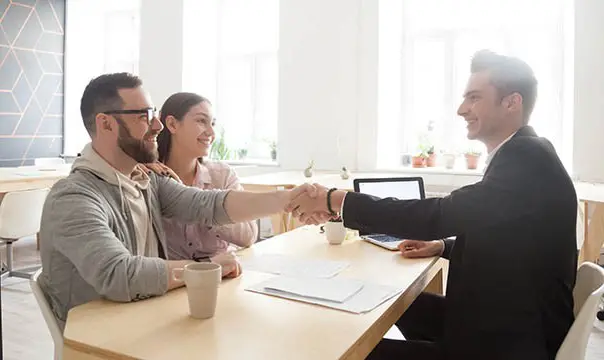 young couple shakes hand of account manager in office
