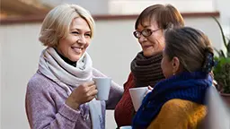 Three women wearing sweaters and drinking tea