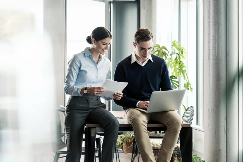 Two professionals looking at a laptop while writing down notes about their retirement plan  