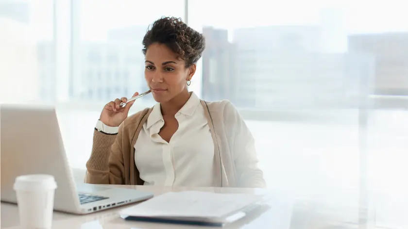 woman sitting at desk reviewing documents on laptop
