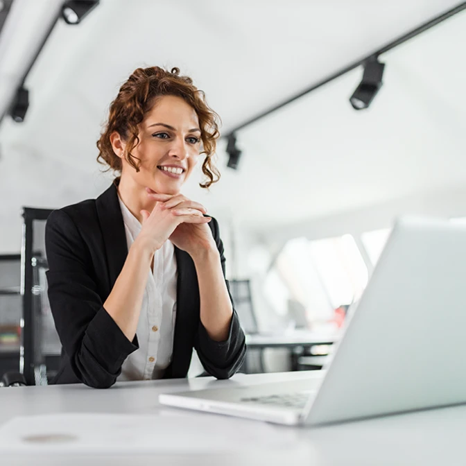 Woman with hands under her chin smiling as she looks at a laptop
