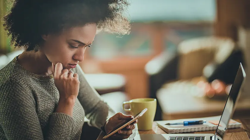 Young woman sitting at her desk with a coffee cup looking at her phone
