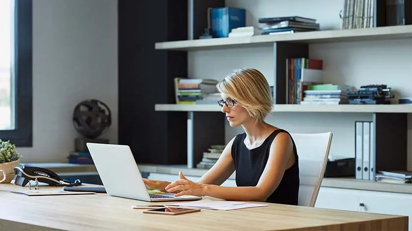 woman wearing glasses working at desk typing on laptop