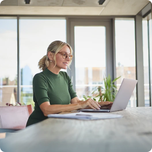 Middle aged woman looking at investments on her laptop by a window 