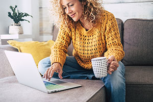 Woman holding a coffee cup and looking at her laptop 