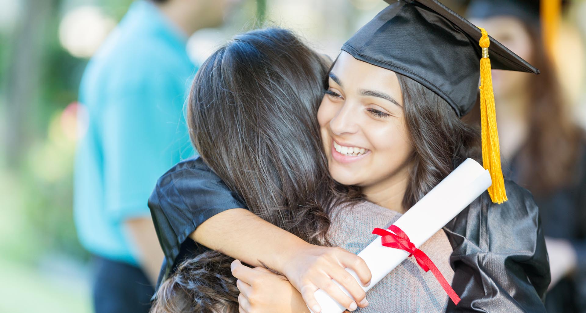 Young woman in her cap and gown, holding her diploam, hugging a parent
