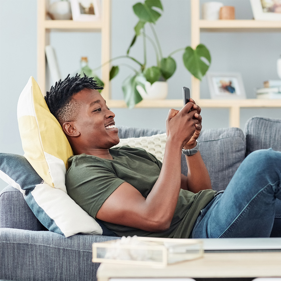Young black man lying on a couch using his cell phone
