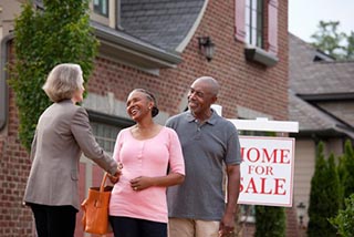 Married couple shaking hands in front of a home for sale sign 