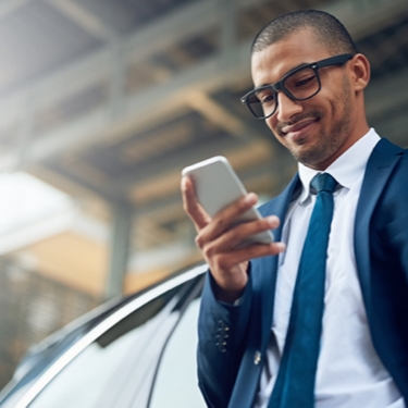 A person standing outside of a car while holding a mobile phone