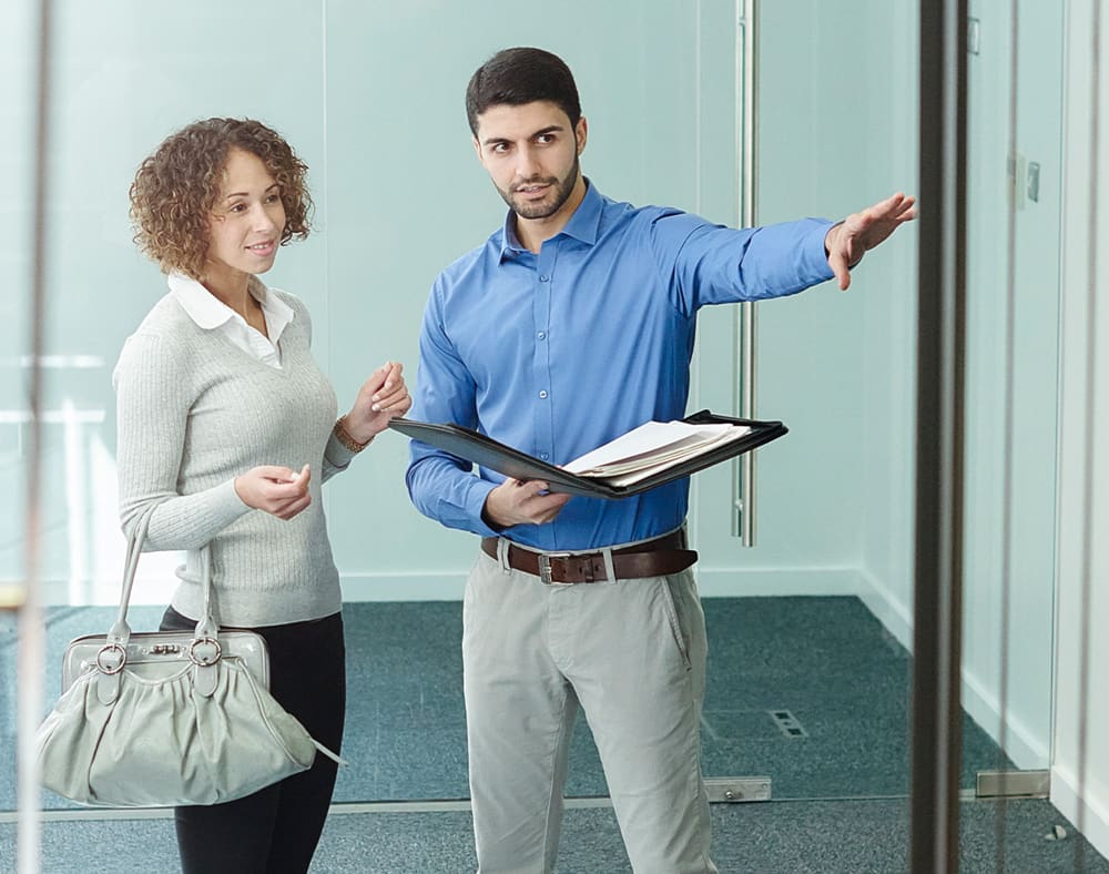 Man holding a portfolio of documents and showing a commercial property to a woman.