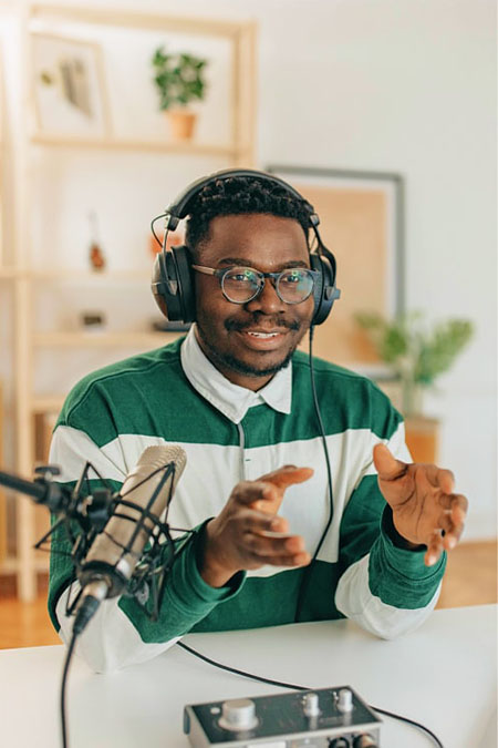 A young Black man sits at his desk recording a podcast.