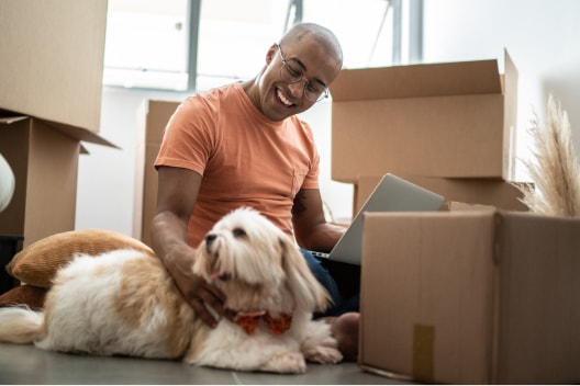 A young Black man unpacks boxes in his new home, his dog by his side.