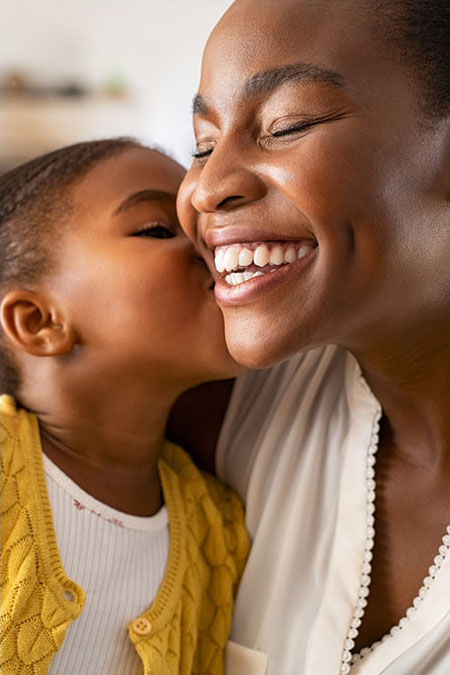 A Black child gives her mother a kiss.