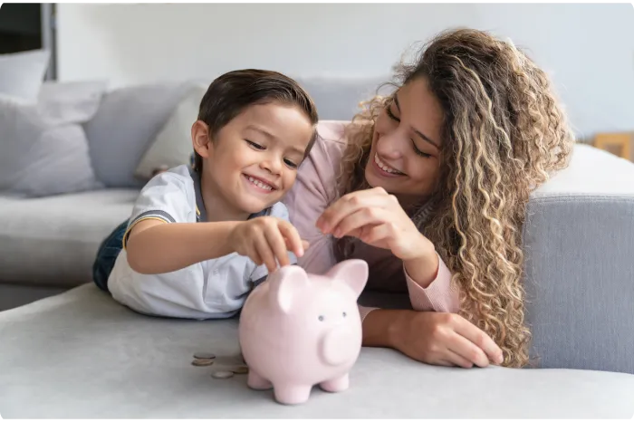 Woman putting coins in to a piggy bank with her young son.