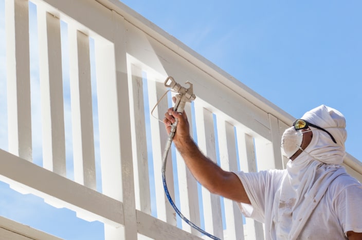 Man in protective gear painting deck railing