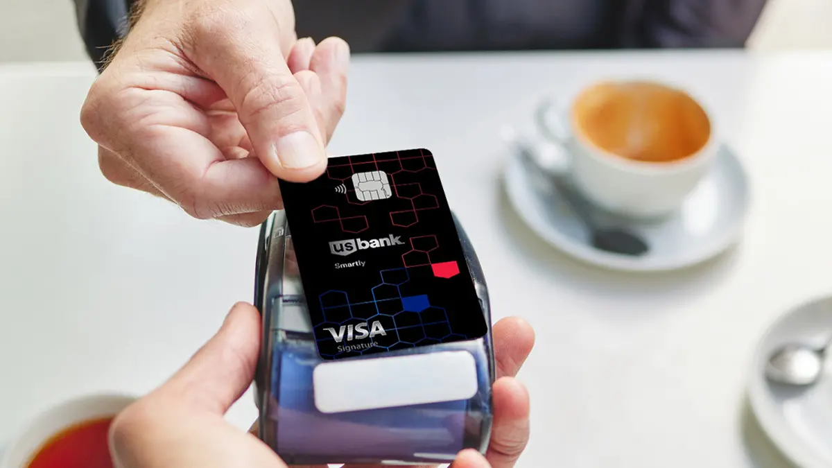 Photo of a credit card tapping a mobile card reader for payment with a cup of coffee in background.