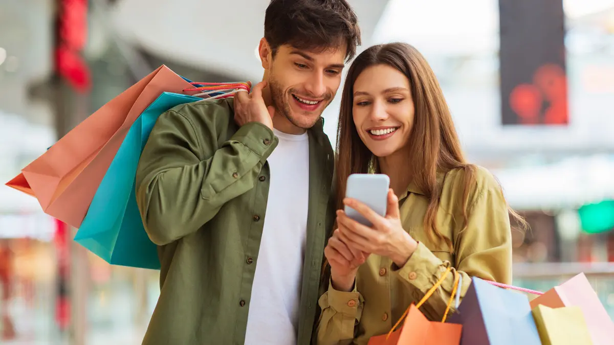Man and woman with shopping bags looking at mobile phone and smiling