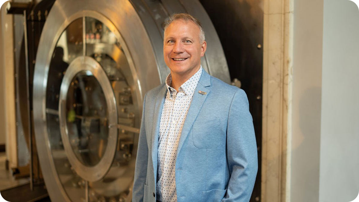 Man standing and facing the camera with a bank vault behind him